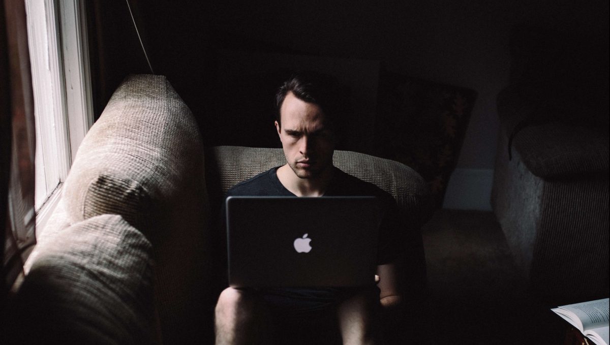 man sitting with a laptop in a dark room wondering why his excuses make him unhappy